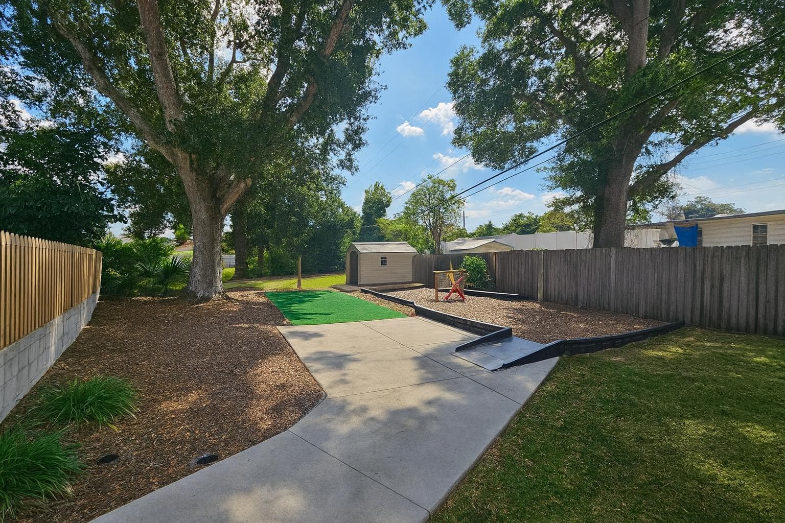 Enjoy a spacious outdoor area perfect for relaxation and gatherings! This charming setting features lush greenery surrounded by tall trees, providing a peaceful retreat right outside your door. The ample space invites you to host barbecues or simply unwind in the sun.
