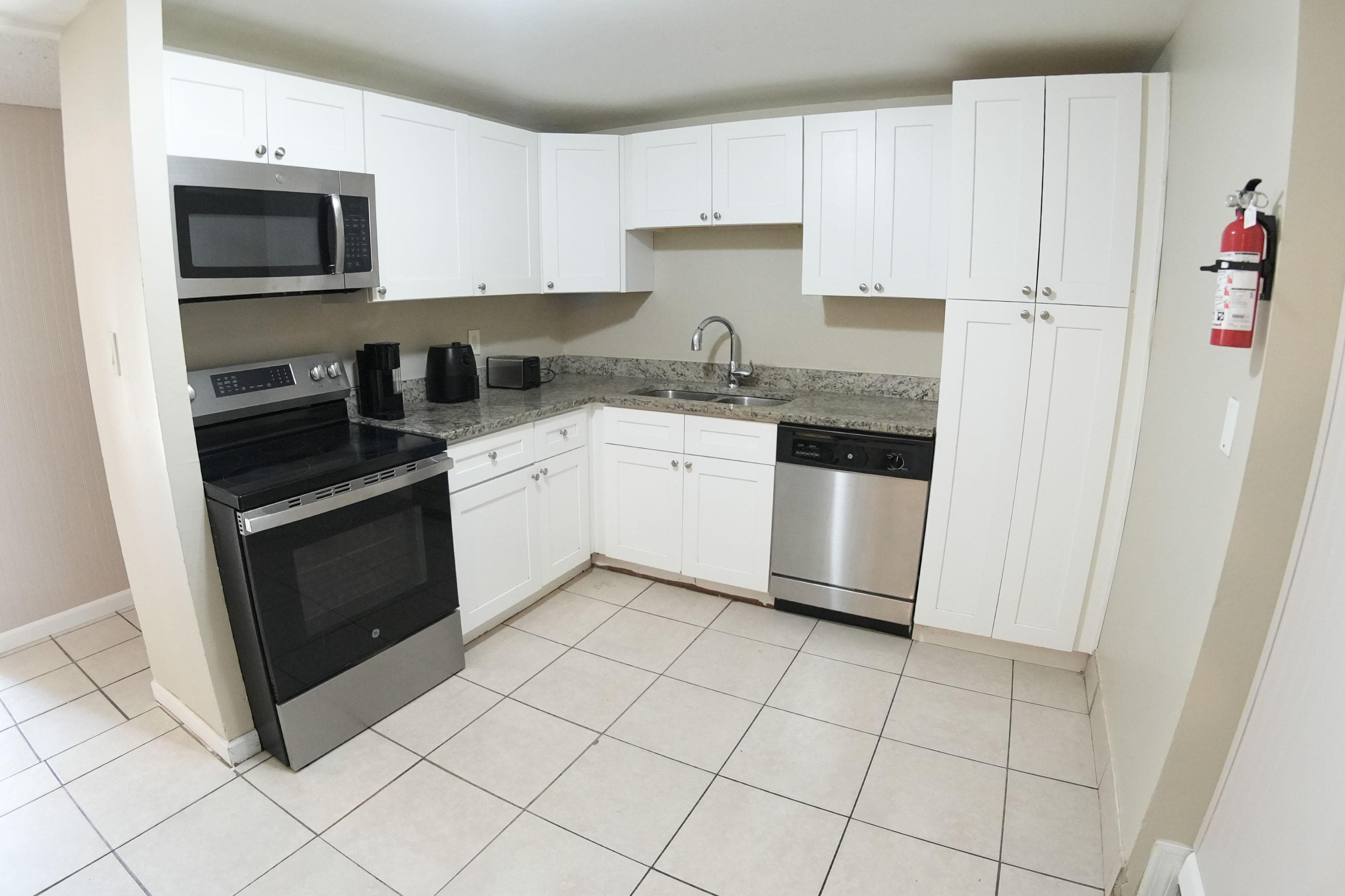 This sleek and modern kitchen features pristine white cabinetry, stylish granite countertops, and stainless steel appliances. It's perfect for preparing meals and entertaining friends in your new coliving space!