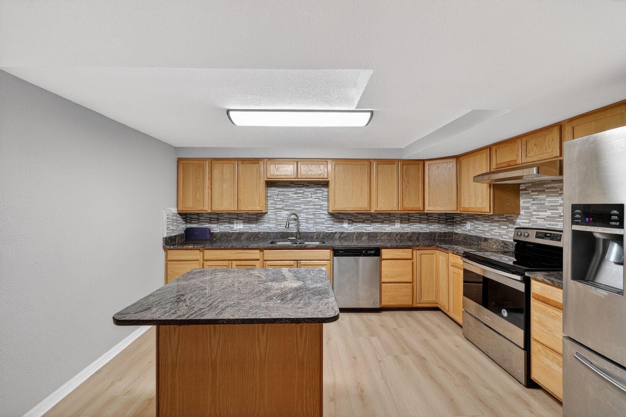 Welcome to this modern kitchen featuring sleek wooden cabinetry and a stunning granite countertop island. The open layout provides ample space for meal prep and gatherings, while the stylish backsplash adds a touch of elegance. It's perfect for those who love to cook and entertain!