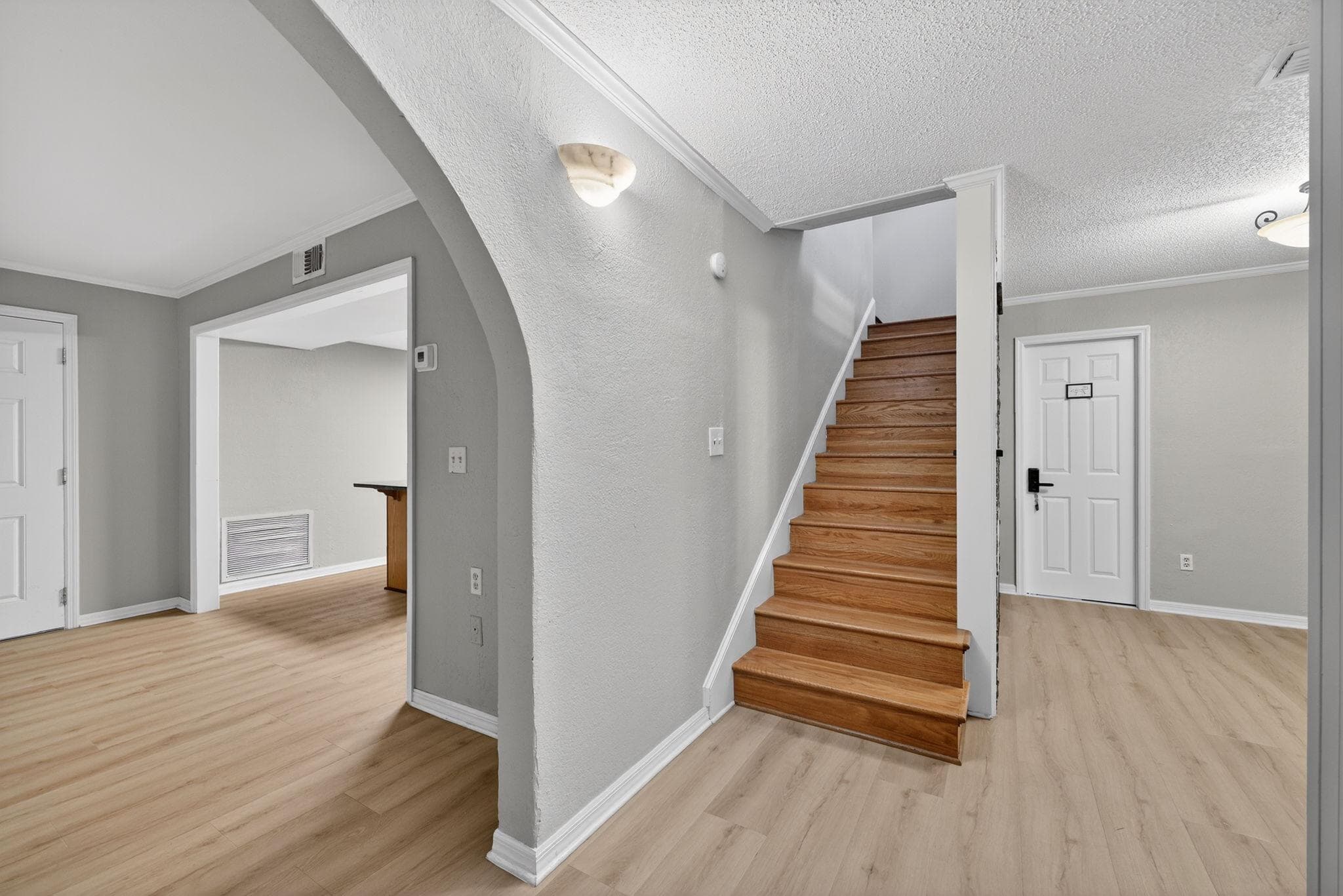 Welcome to your future home! This inviting hallway features warm wooden stairs leading up to the living areas, bathed in soft natural light. The neutral color palette creates a calming atmosphere, perfect for unwinding after a long day. Imagine the possibilities of personalizing this space!