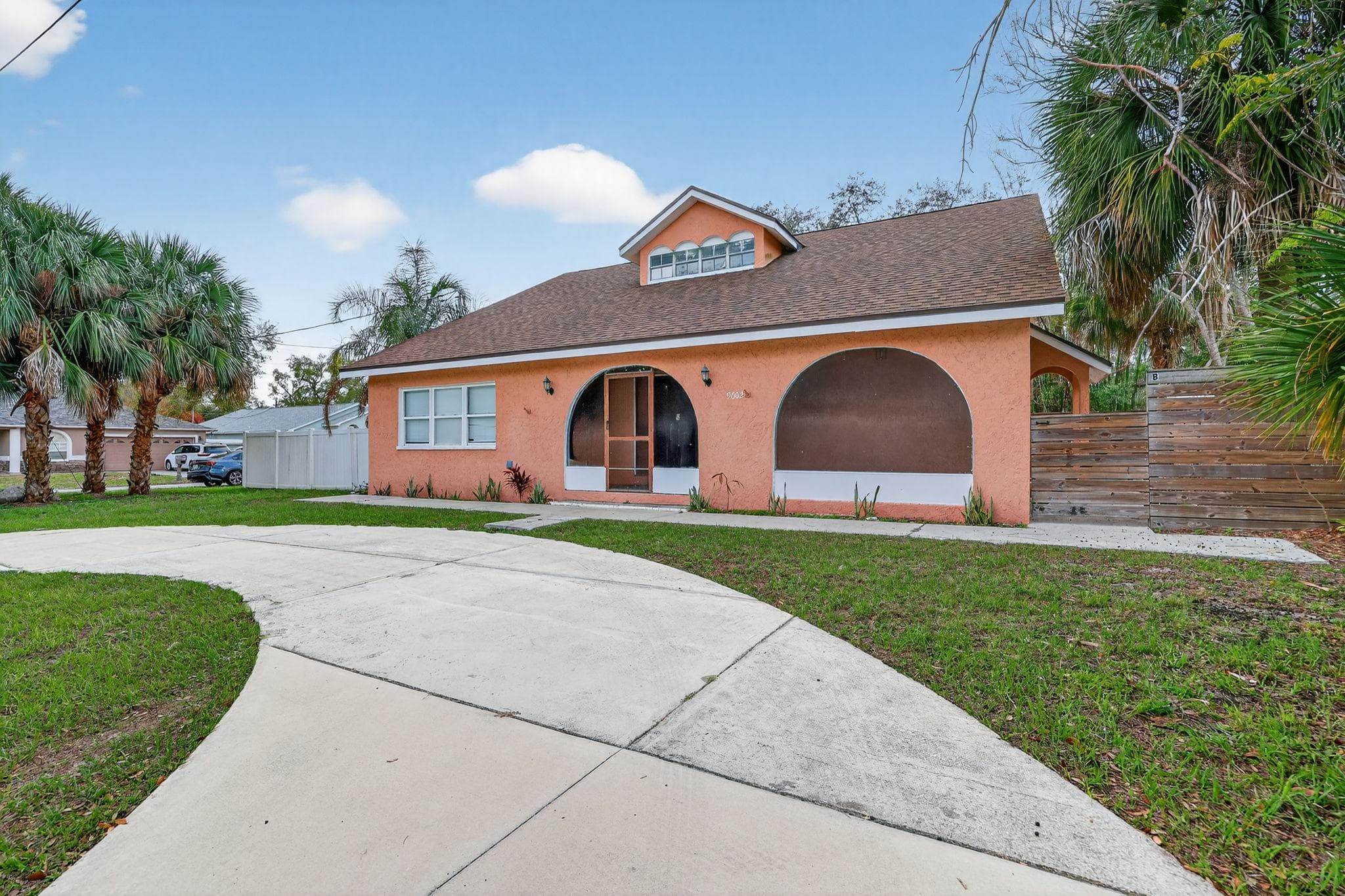 Welcome to your potential new home! This charming exterior showcases a vibrant orange façade surrounded by lush greenery and palm trees, creating a warm and inviting atmosphere. The spacious driveway offers convenience and ease of access, perfect for hosting friends or digging into some outdoor activities. Imagine relaxing here after a long day!