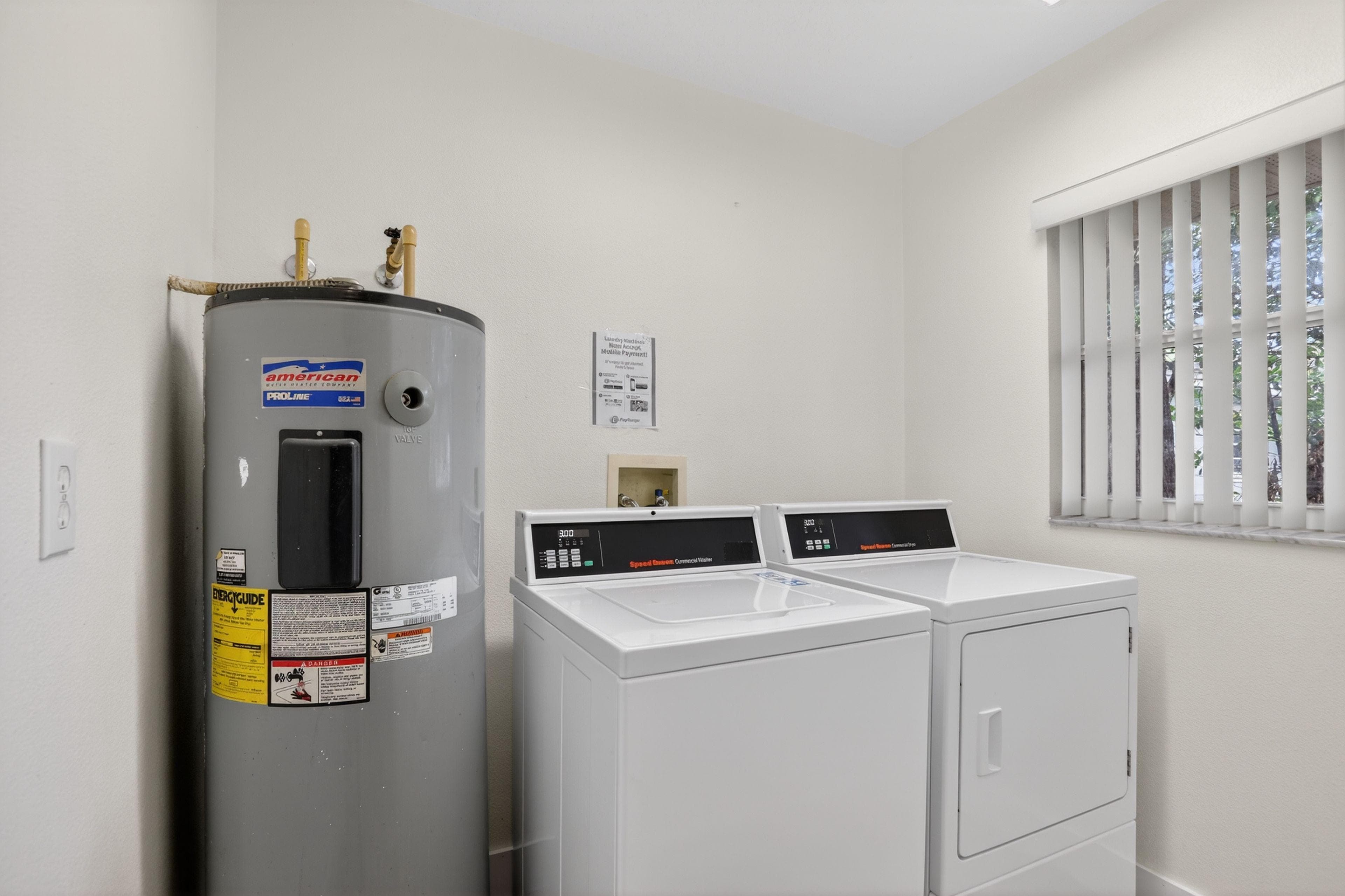 Clean, bright laundry area featuring a full-size washer and dryer with a nearby water heater and a window with blinds for natural light and ventilation. A practical, well-kept utility space that makes everyday chores convenient.