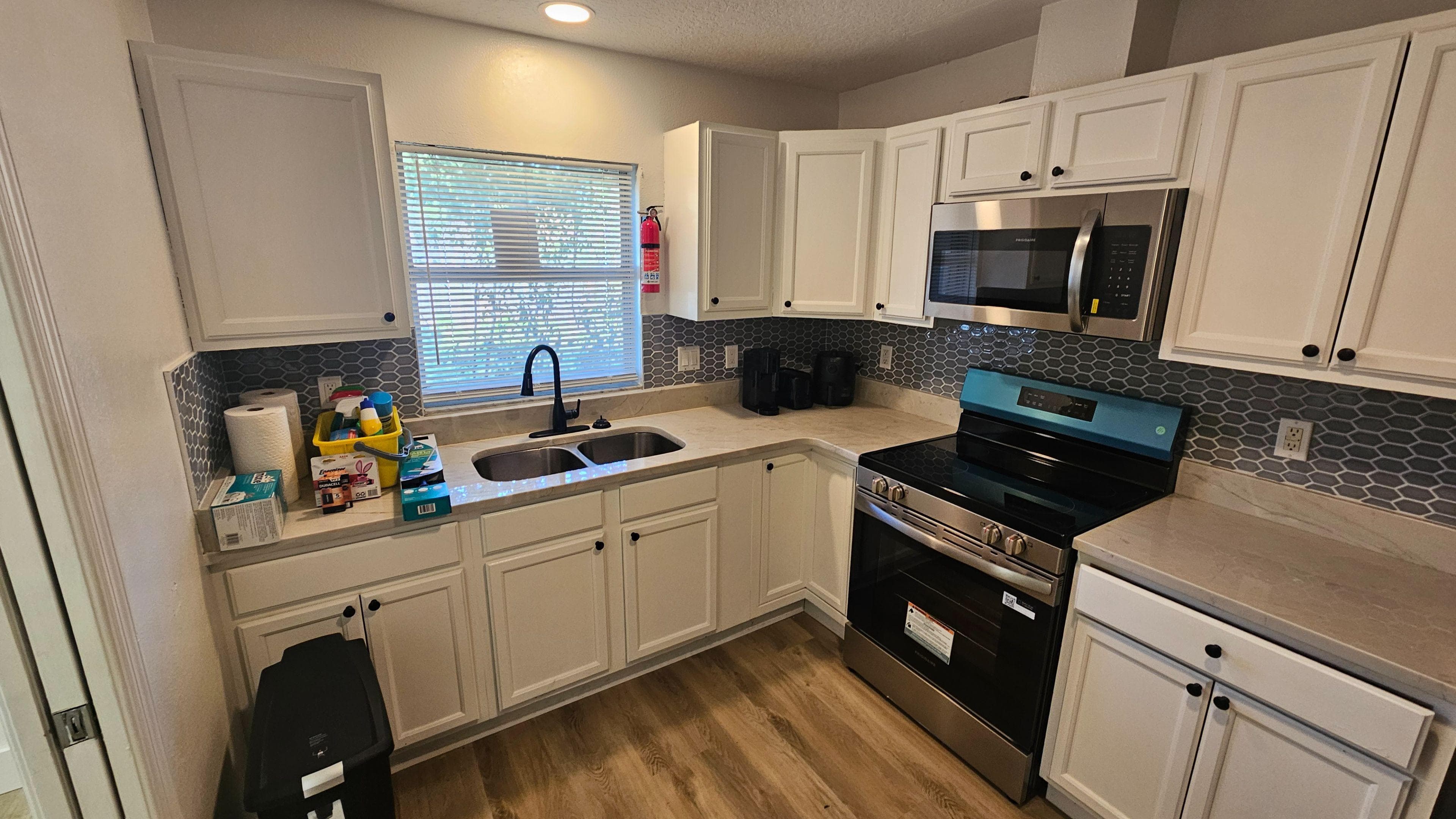 Bright, updated kitchen featuring crisp white cabinetry, a modern gray tile backsplash, and stainless steel range and microwave for everyday convenience. The double-basin sink sits beneath a window for great natural light, with ample counter space and storage for meal prep and shared living.