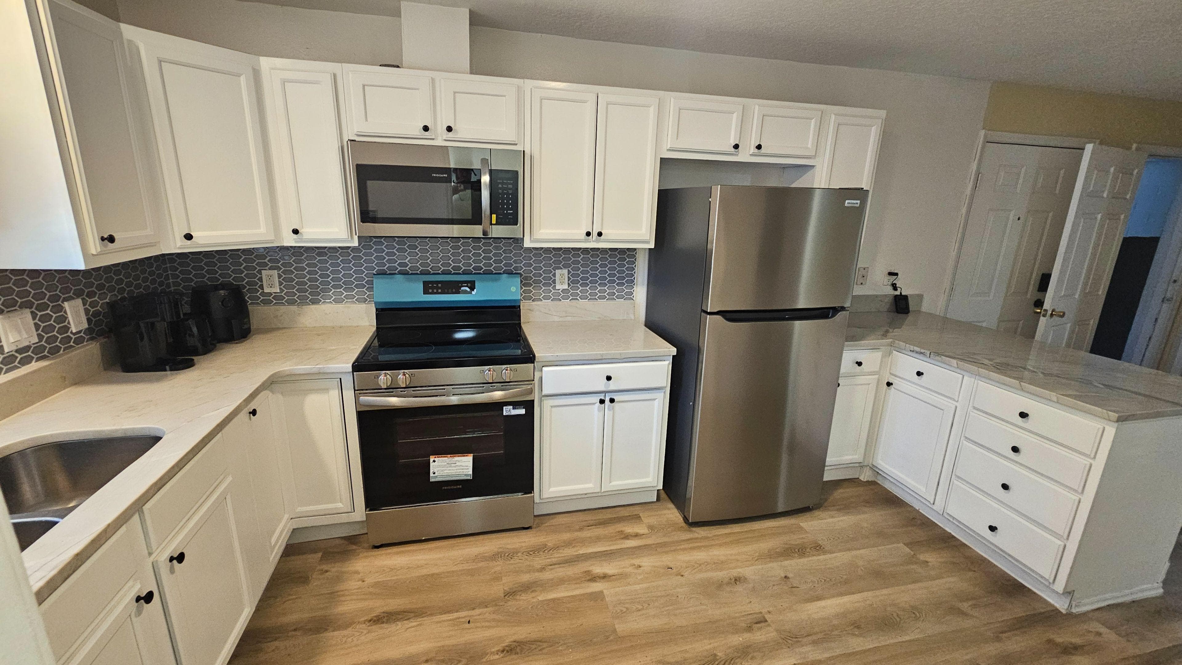 Bright, updated kitchen featuring crisp white cabinetry, modern stainless-steel appliances, and a stylish hex-tile backsplash. Generous countertop space and a functional U-shaped layout make everyday cooking and meal prep easy.
