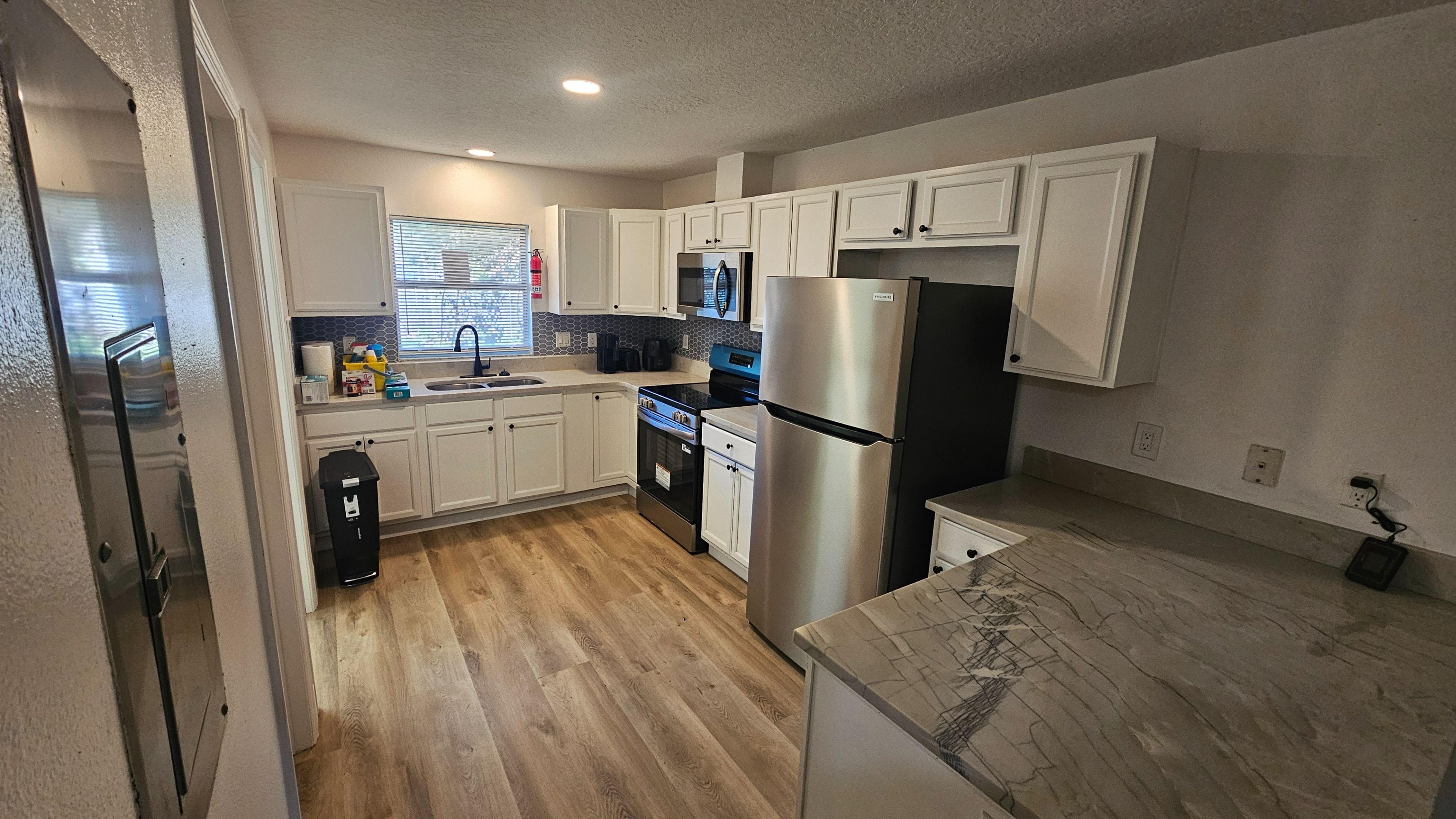 Bright, modern kitchen featuring crisp white cabinetry, stainless-steel appliances, and a stylish tile backsplash, with a window over the sink bringing in natural light. Ample counter space and updated flooring make meal prep and everyday living feel easy and comfortable.