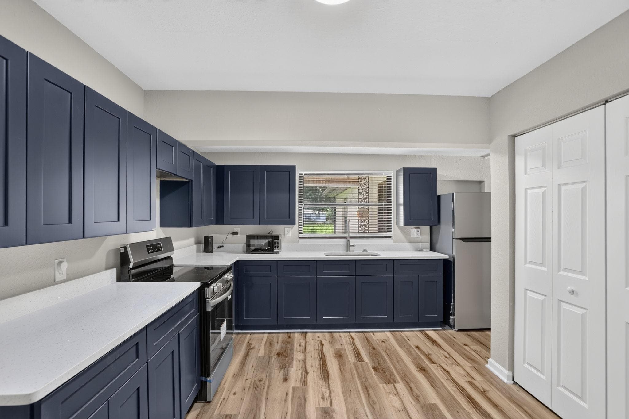 Updated kitchen with ample navy cabinetry, generous counter space, stainless appliances, and a window over the sink.