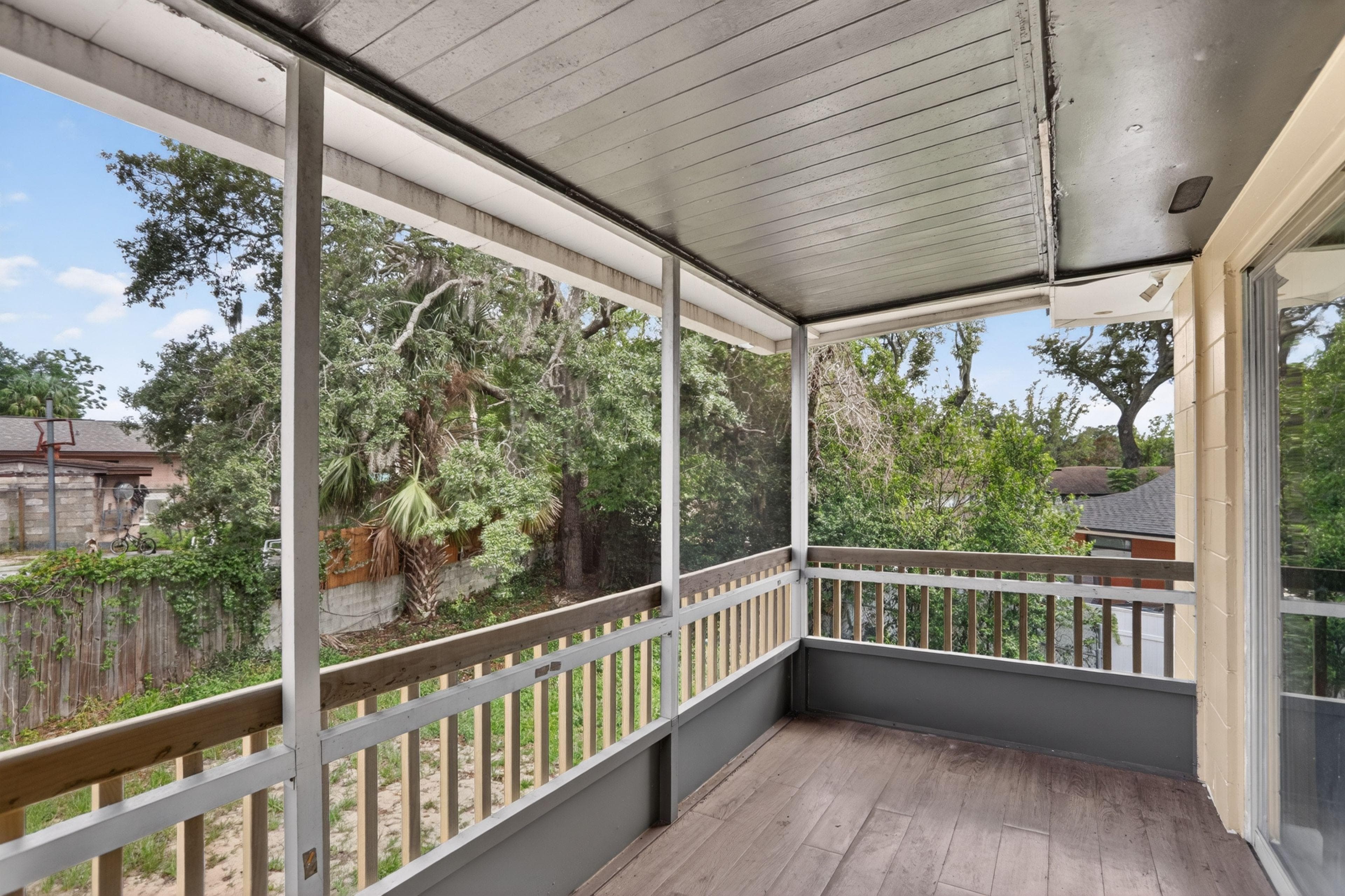 Covered screened porch with wood-look flooring and railing, offering treetop views and a shaded spot to relax outdoors.