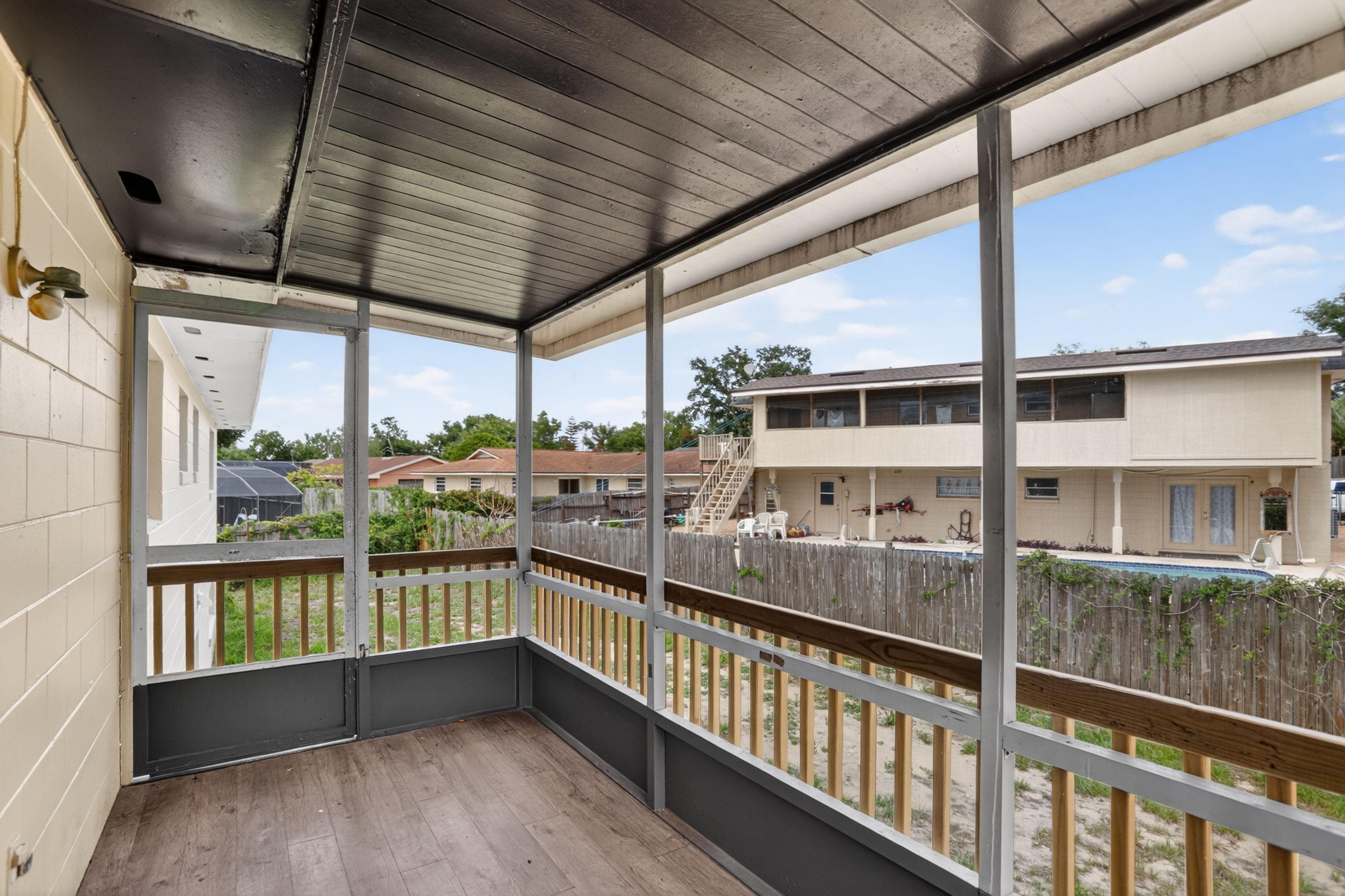 Covered screened porch with wood-look flooring and railing, offering an elevated outdoor space overlooking the yard.