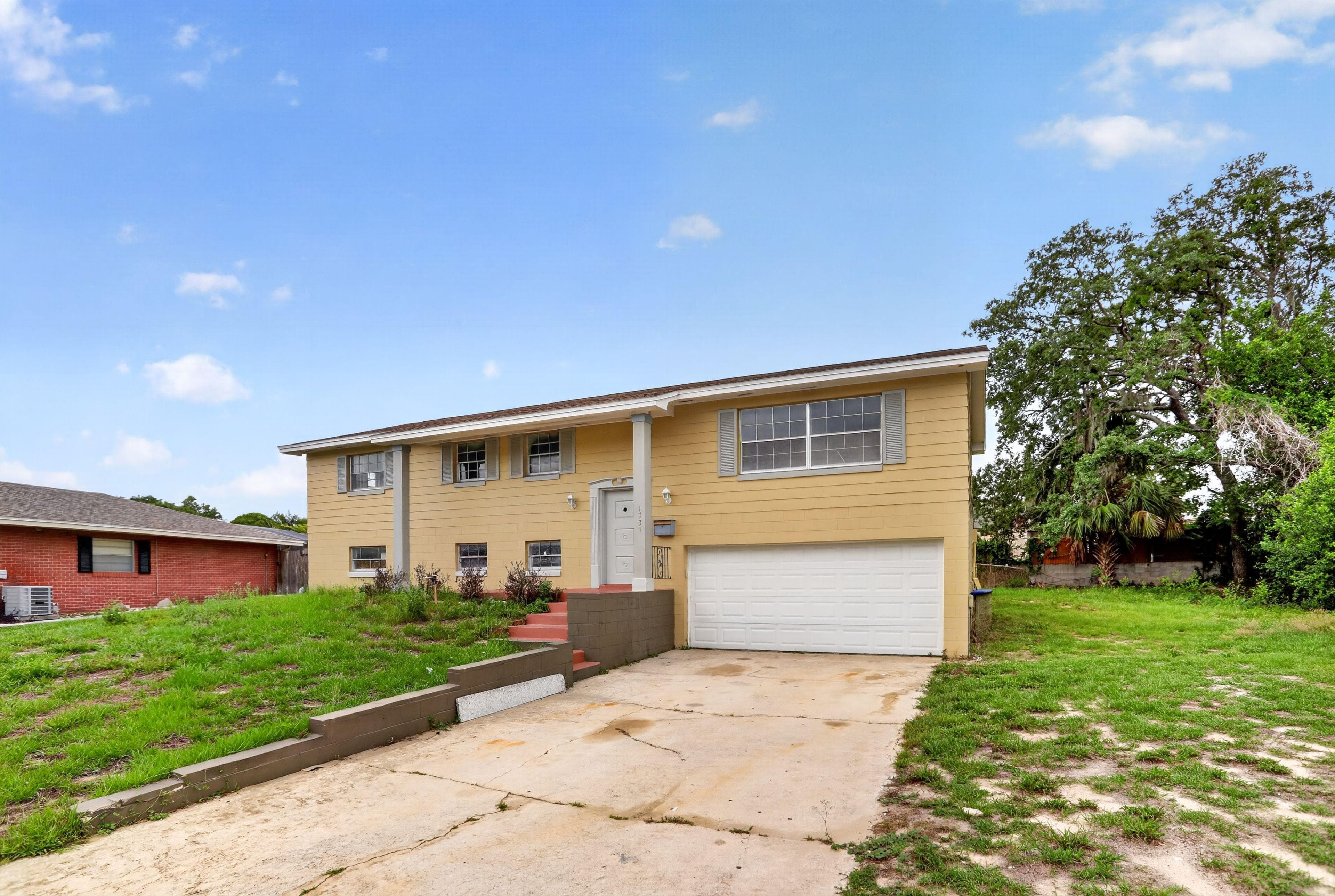 Split-level home with an attached garage, driveway parking, and a spacious front lawn with mature trees.