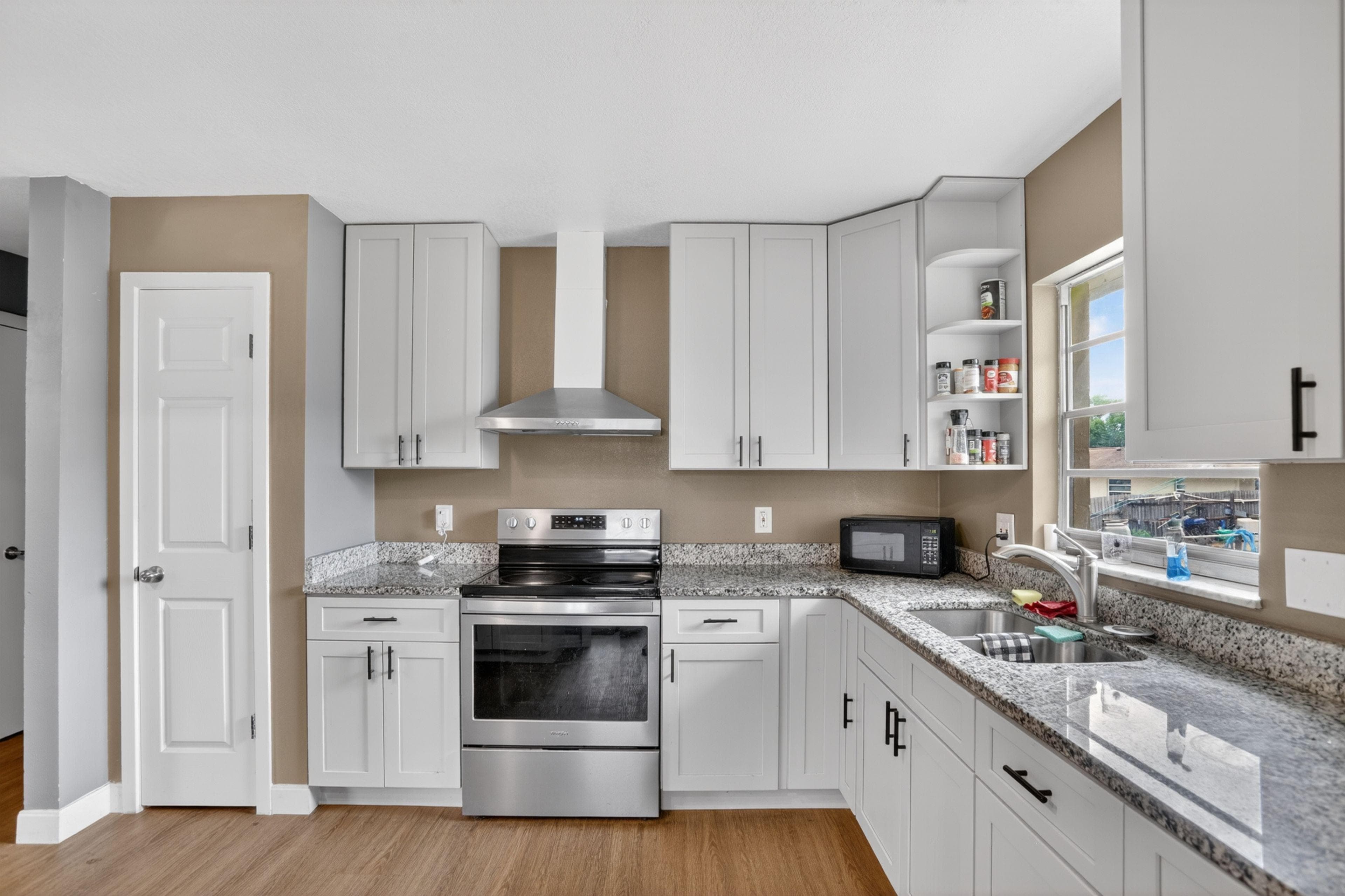 Updated kitchen with shaker-style cabinetry, granite countertops, stainless range/hood, and an L-shaped sink area with window