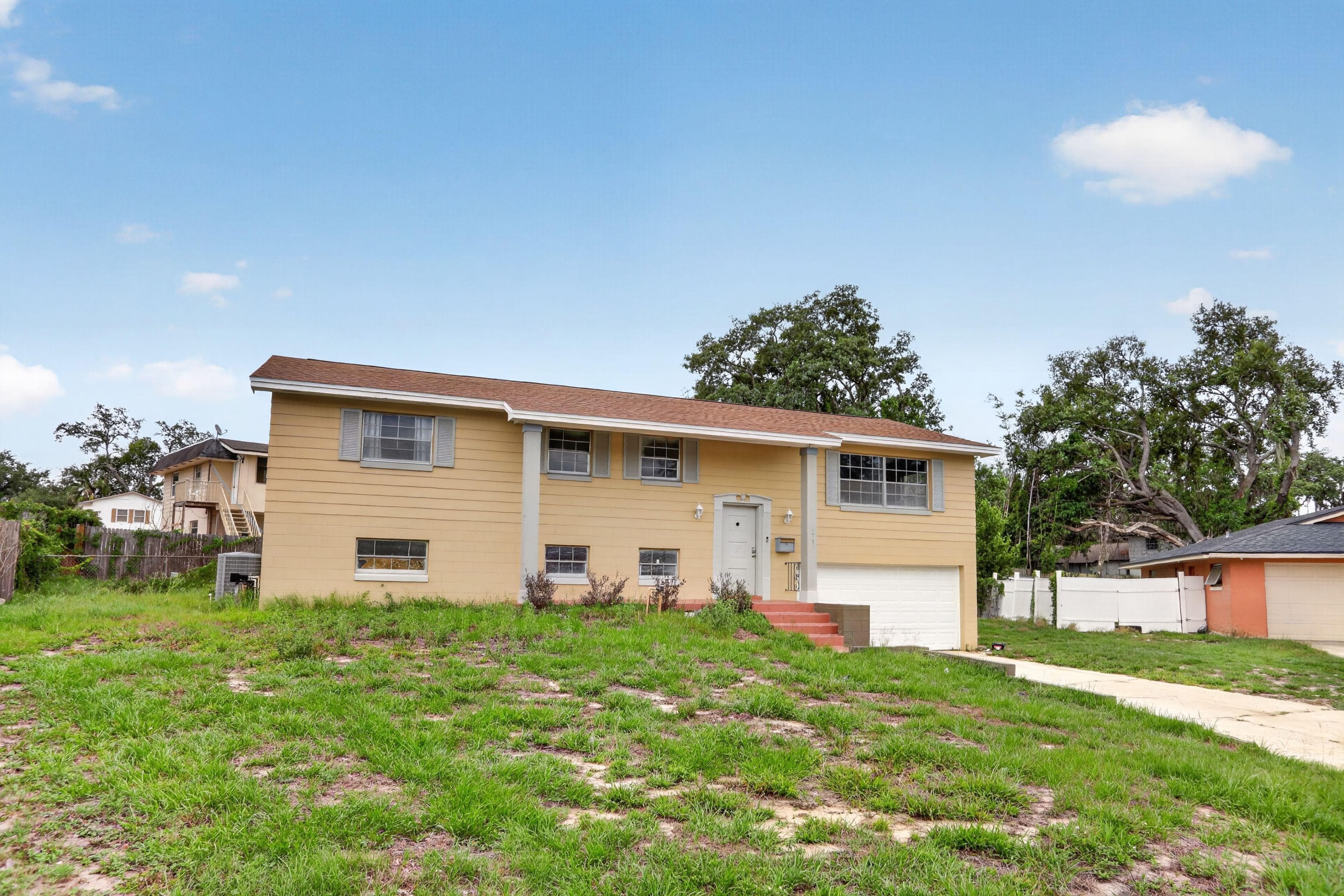 Raised single-family home with a one-car garage, covered entry, and large front lawn with a paved walkway.