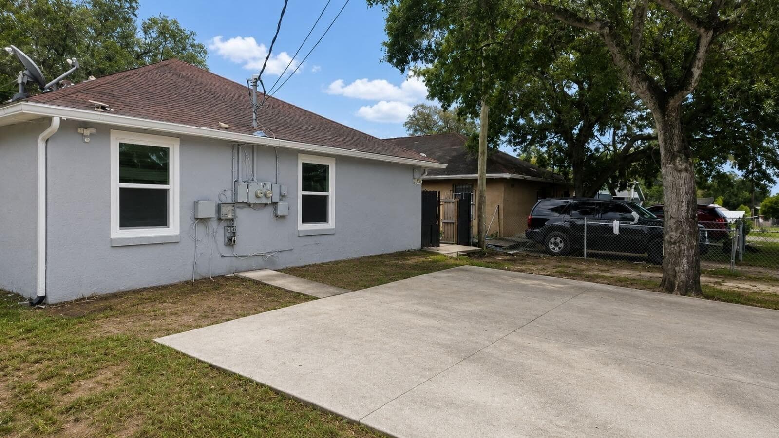 Side yard features a wide concrete driveway for off-street parking and a fenced area with mature shade trees.